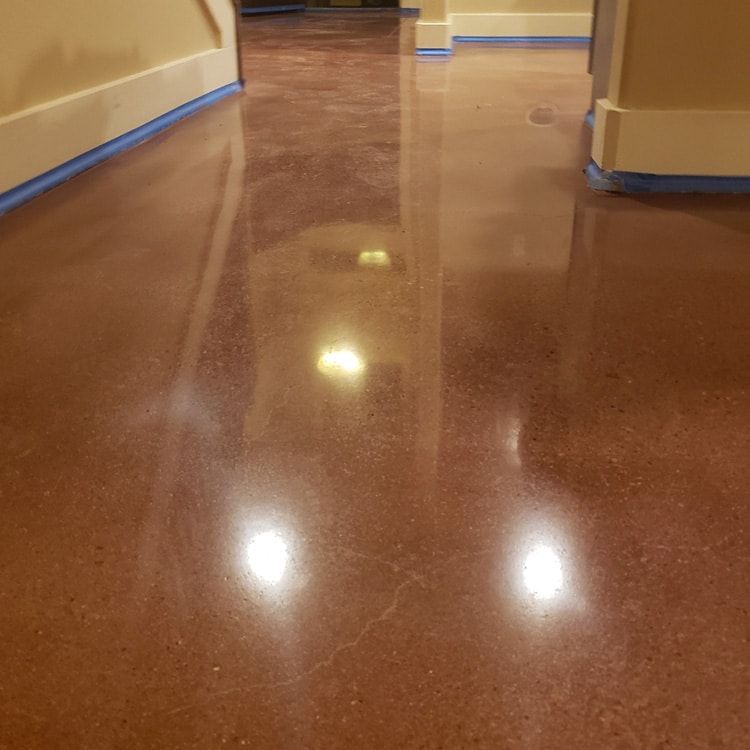 Shiny brown epoxy flooring with light reflections, flanked by walls with blue painter's tape at the base.
