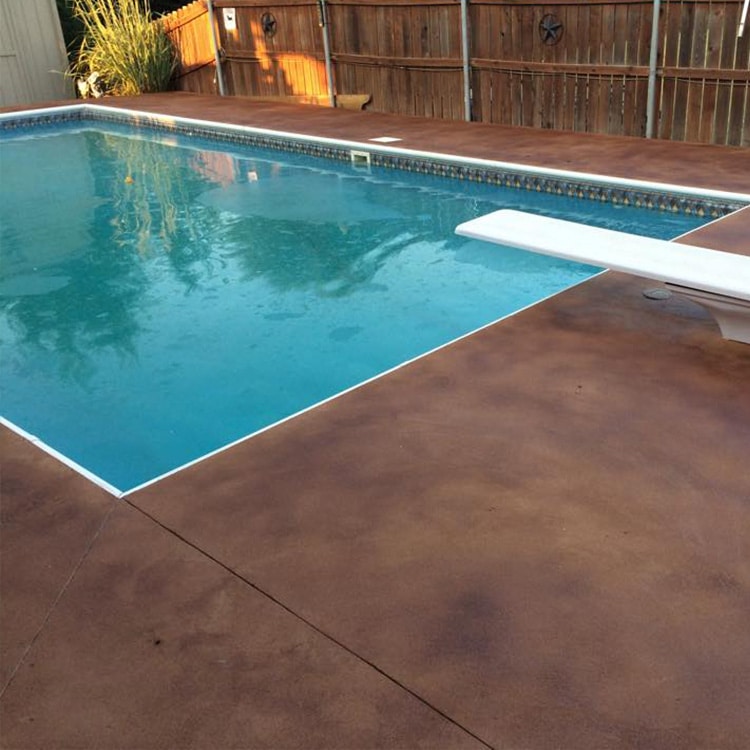Swimming pool with clear blue water adjacent to a stained concrete deck, surrounded by a wooden fence.